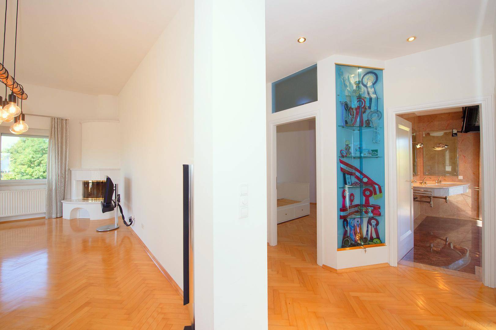 Heller Flur mit Fischgrätparkett, dekorativer Vitrine und Zugang zu Wohnzimmer und Bad.