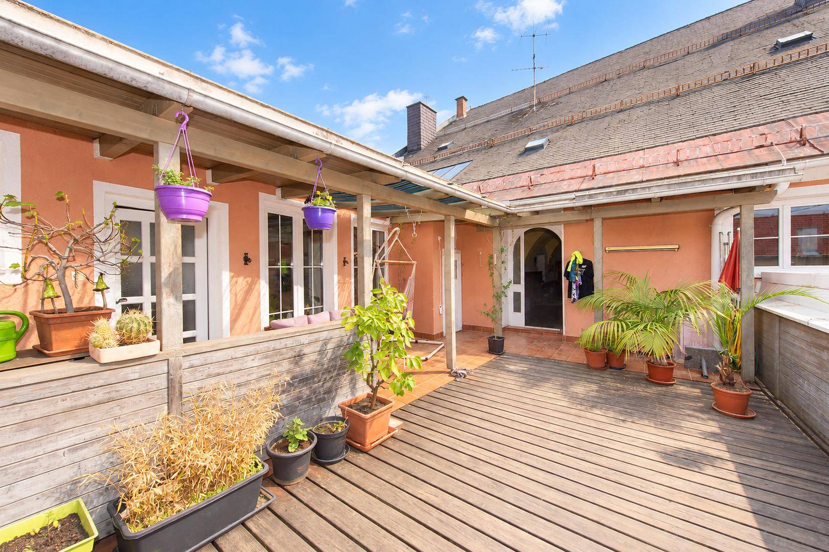 Dachterrasse mit Holzdeck, vielen Pflanzen und Zugang zu den Innenräumen.
