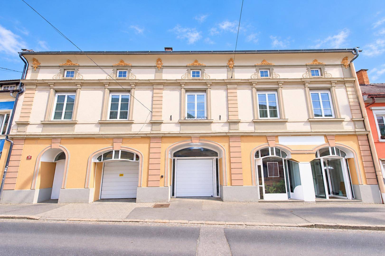 Historisches Gebäude mit mehreren Garagentoren und großen Fenstern an einer Straße, gut erhaltene Fassade.