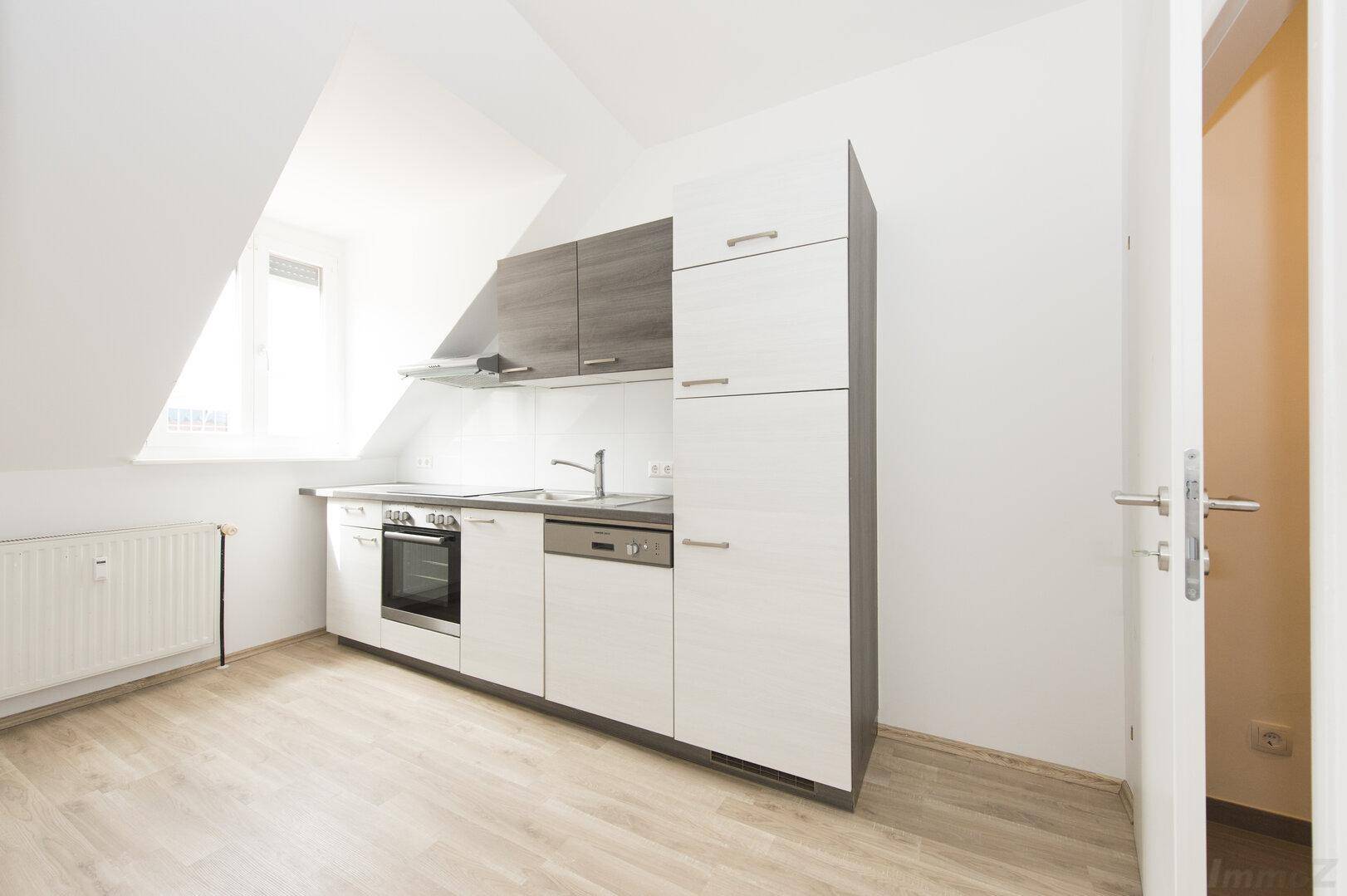 Moderne Einbauküche mit hellen Fronten, Dachschräge und Laminatboden.