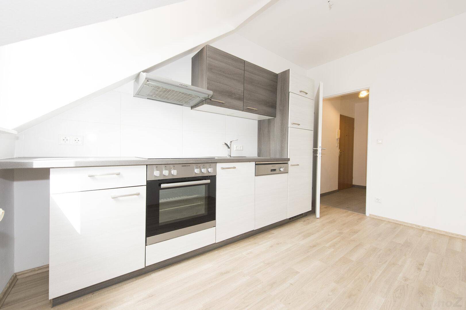 Moderne Küchenzeile mit hellen Schränken, Geräten und Laminatboden in Dachgeschosswohnung.