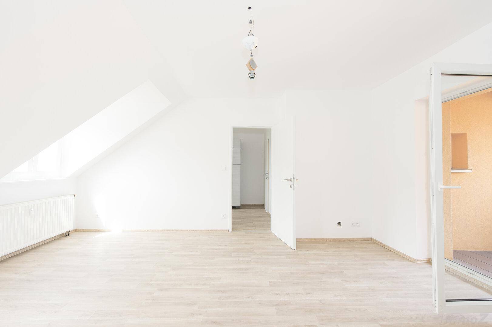 Heller Wohnbereich mit Laminatboden, Dachschräge und Zugang zu einem weiteren Raum.