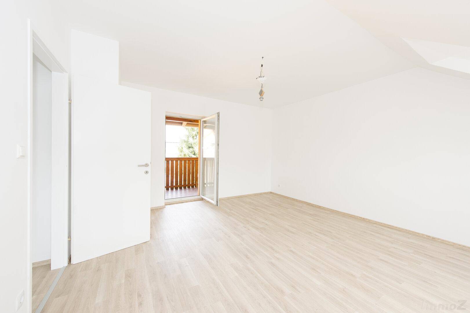 Geräumiger Wohnbereich mit Laminatboden, Dachschräge und offenem Balkonzugang.