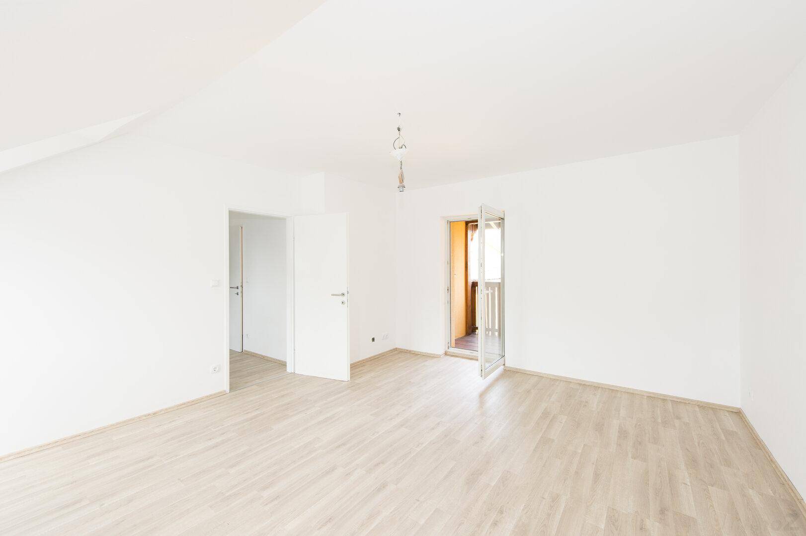 Heller Wohnraum mit Laminatboden, Dachschräge und Zugang zum Balkon.
