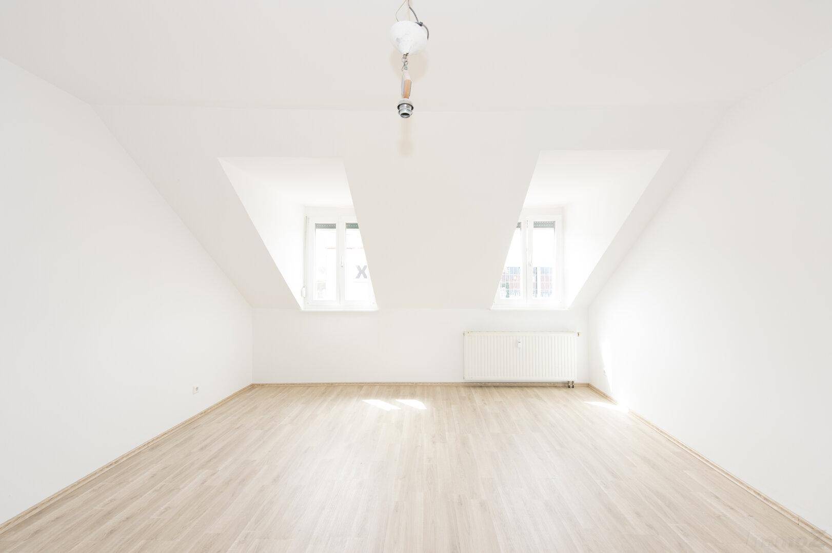 Geräumiger, heller Wohnraum mit Dachschrägen und zwei Fenstern.