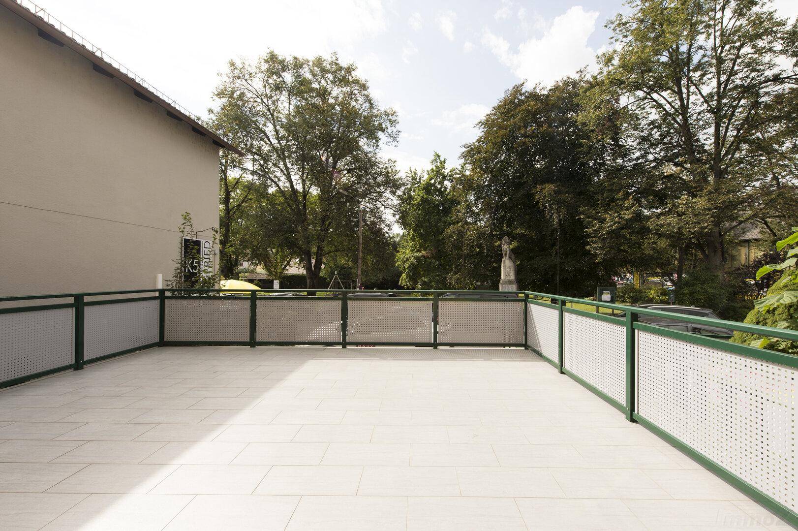 Helle Terrasse mit Fliesenboden und einer grünen Hecke, die Privatsphäre bietet.