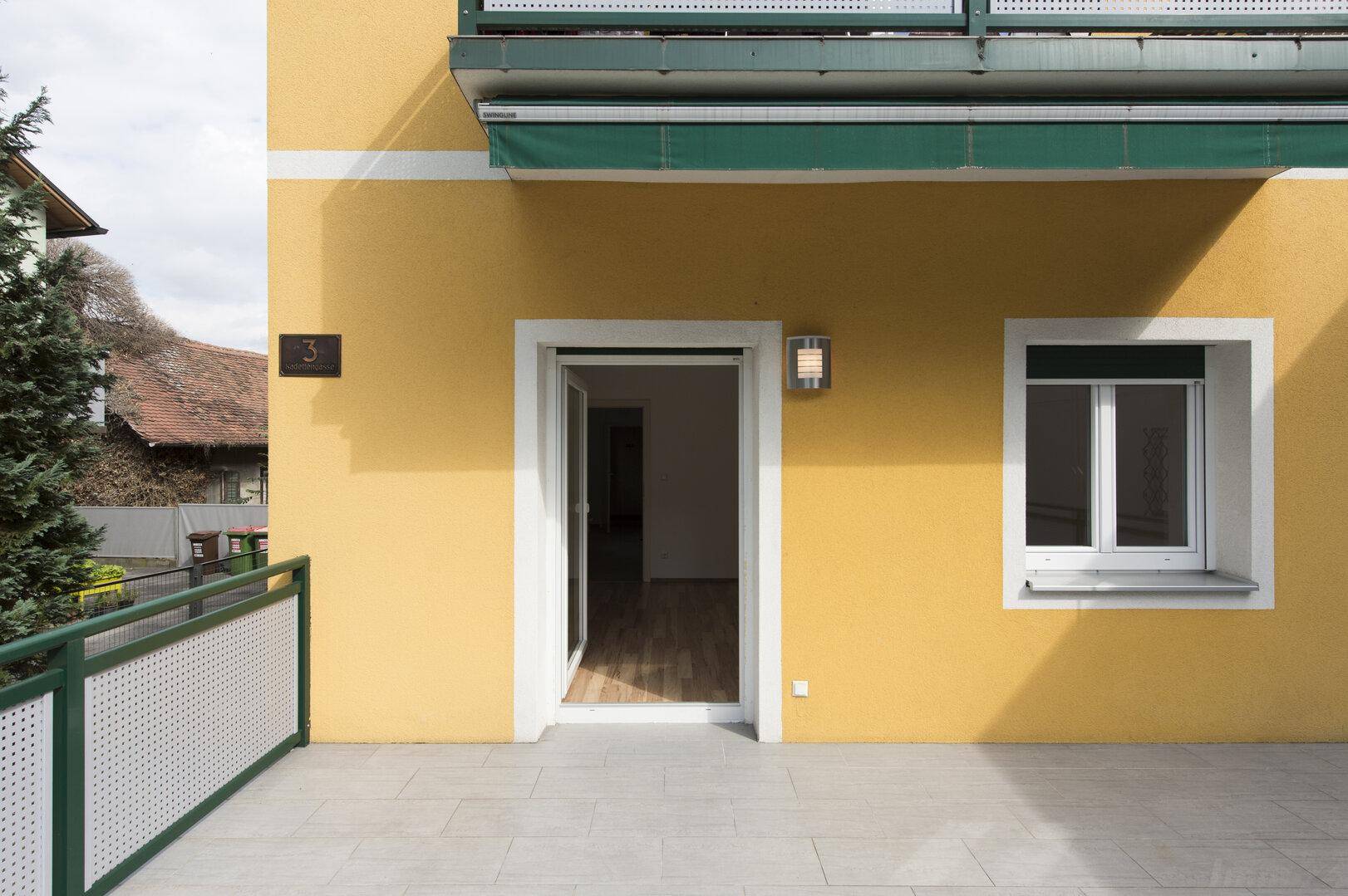 Zugang zur geräumigen Terrasse vom Innenbereich des Hauses, mit heller Fassade.