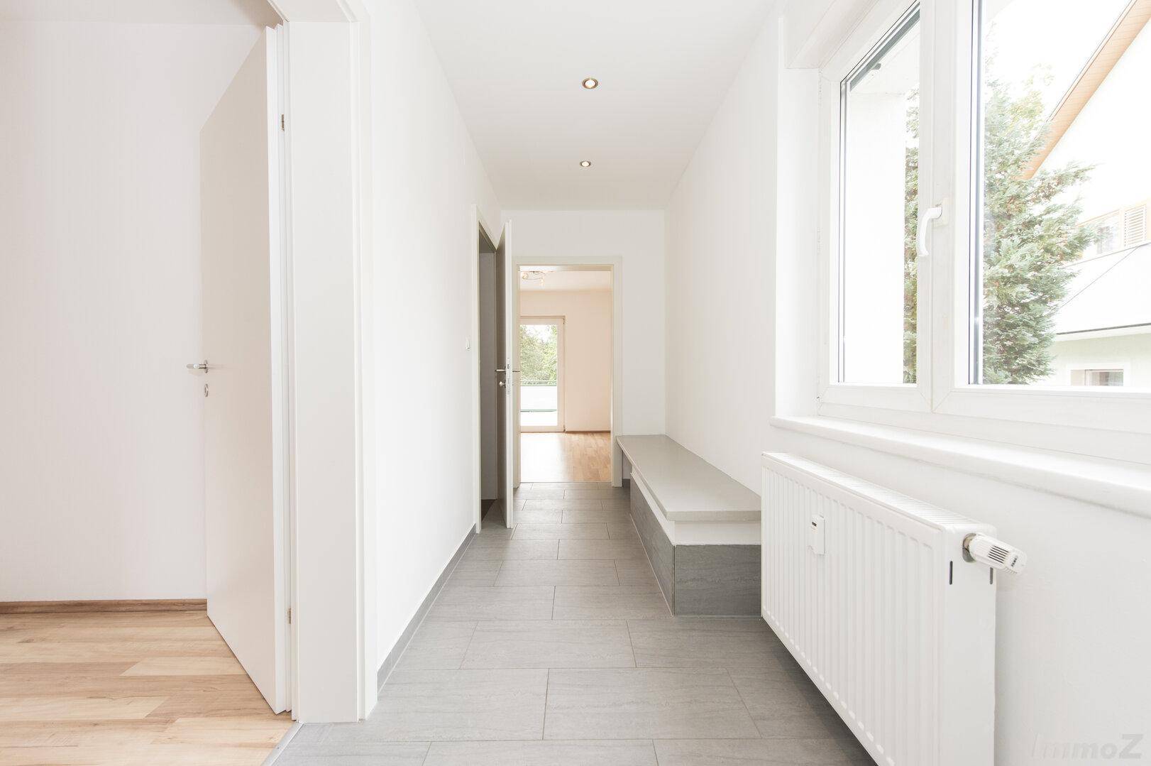 Langer, heller Flur mit Fliesenboden, Einbaubank und Heizkörper unter dem Fenster.