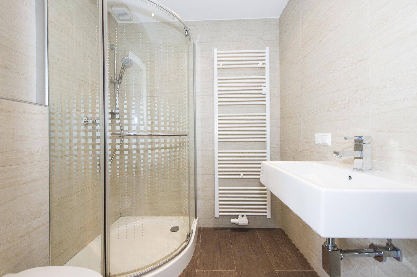 Helles Badezimmer mit moderner Duschkabine, Waschbecken und beheiztem Handtuchhalter.