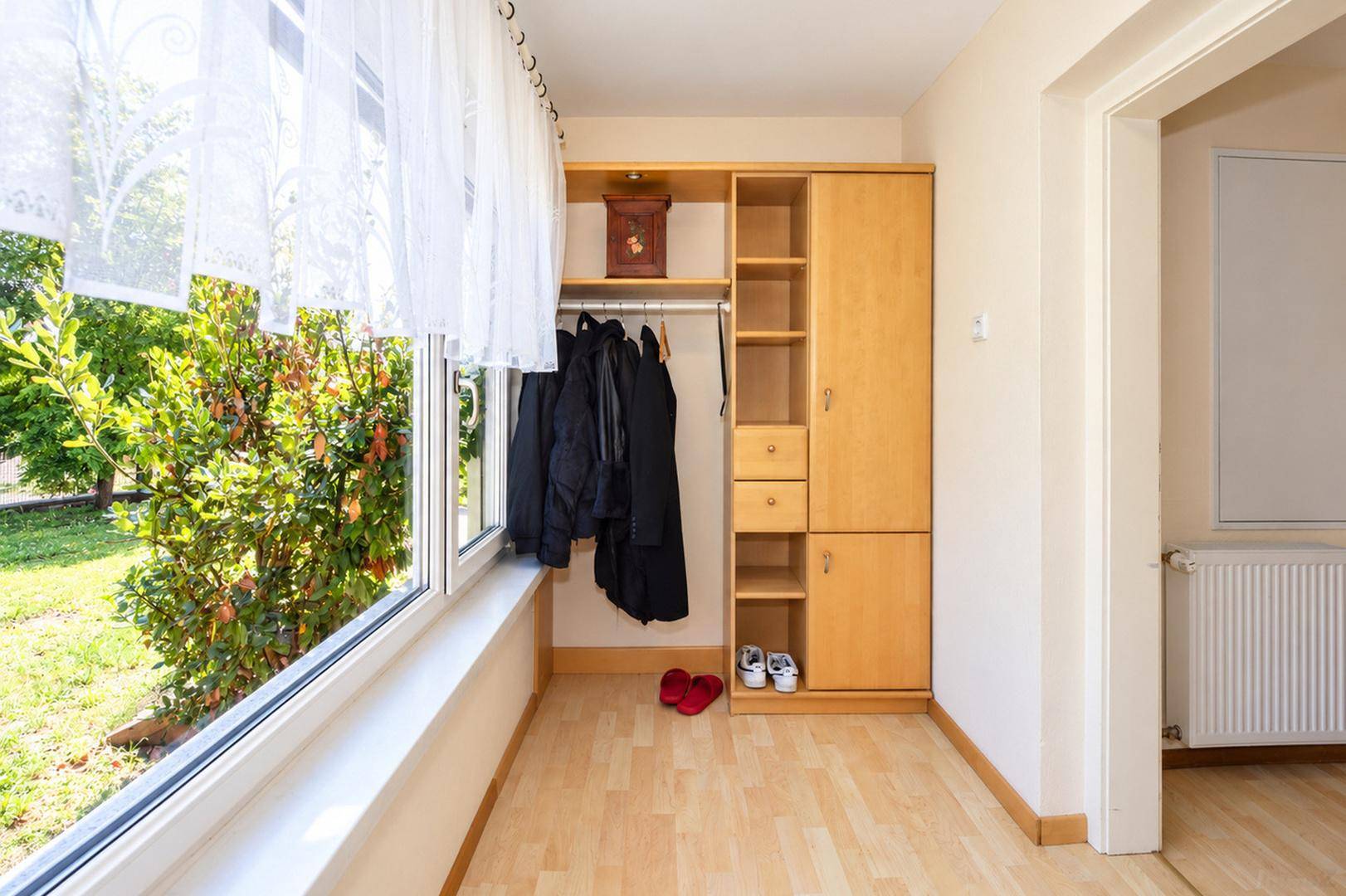 Heller Eingangsbereich mit Holzschrank, Garderobe und großem Fenster mit Blick ins Grüne.