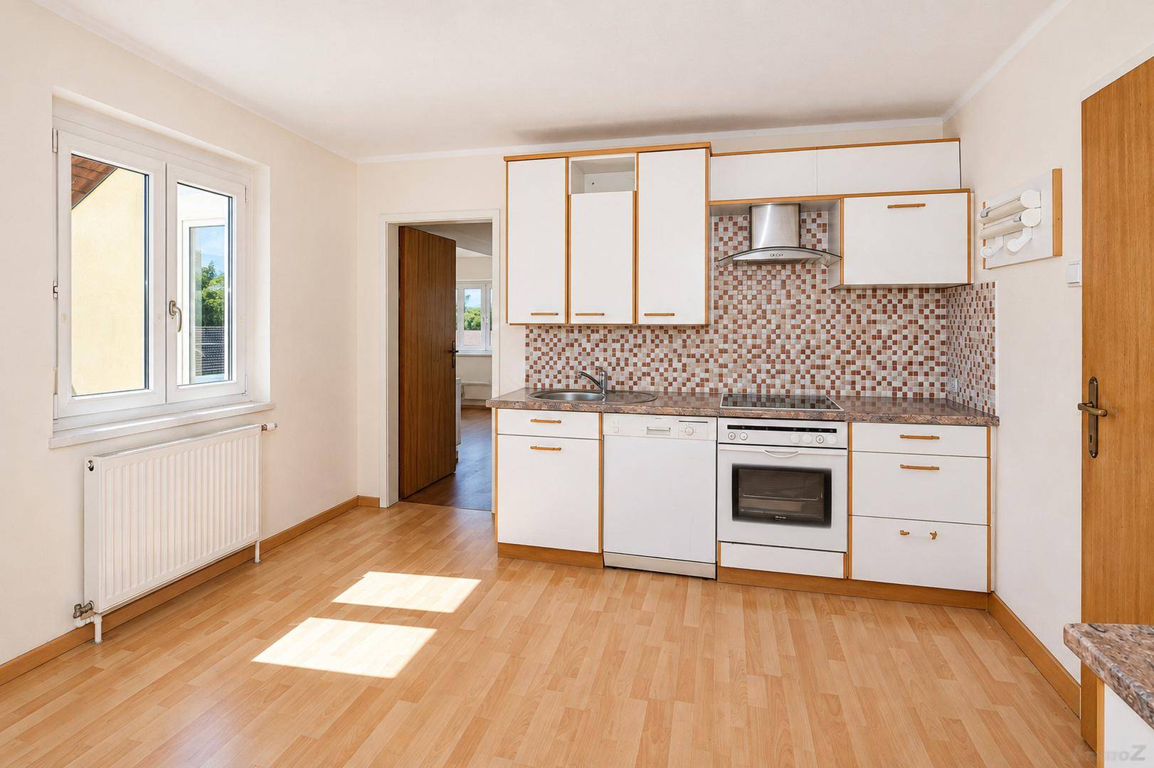 Funktionale Küche mit weißen Schränken, Fliesenrückwand und integrierten Geräten, ausgestattet mit Laminatboden.