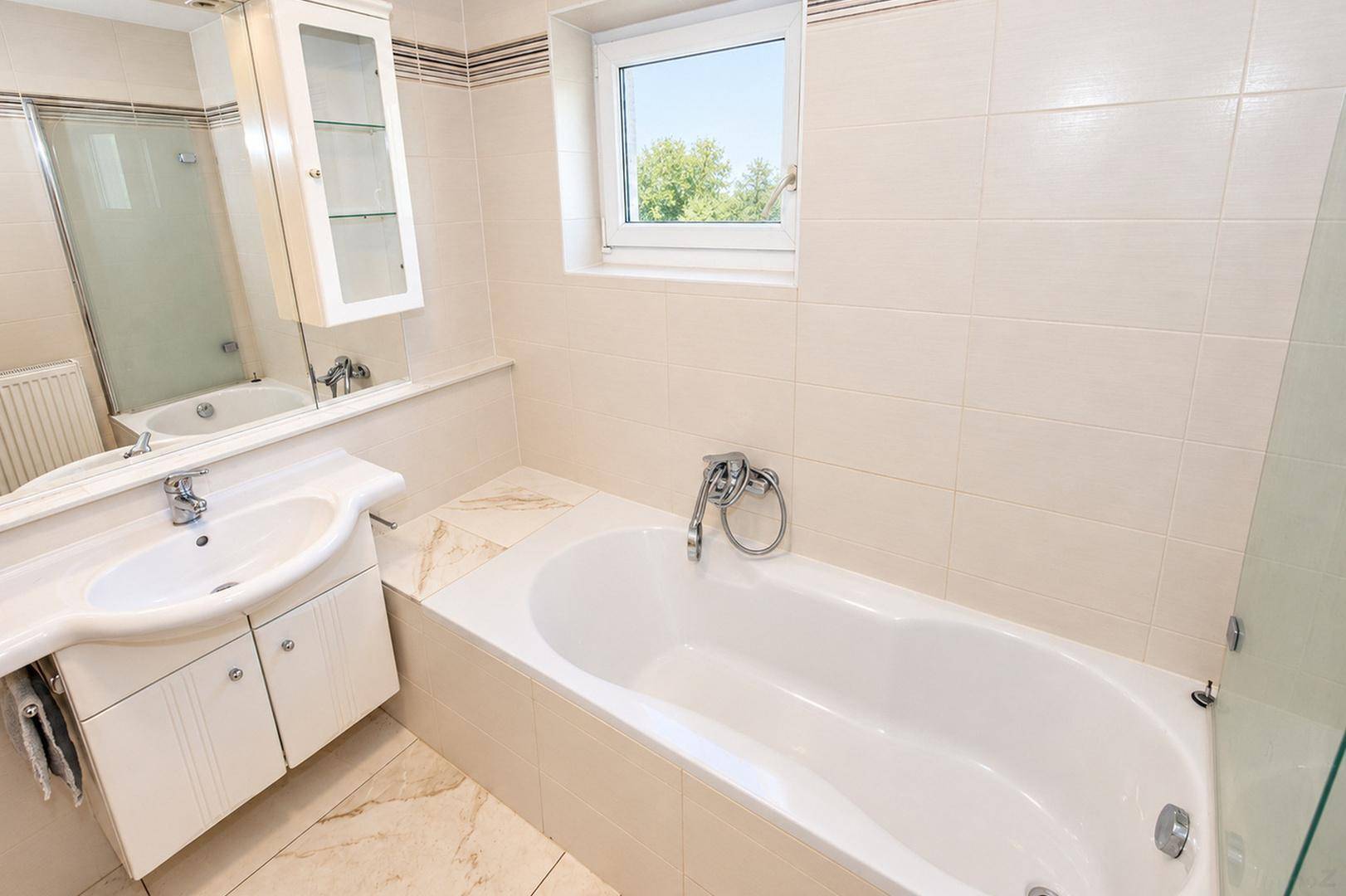 Badezimmer mit Badewanne, Einzelwaschbecken und Fliesenboden, hell und funktional.