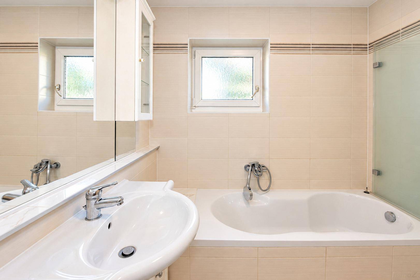 Badezimmer mit Badewanne, Waschbecken und Spiegel, in hellen Fliesen gehalten.