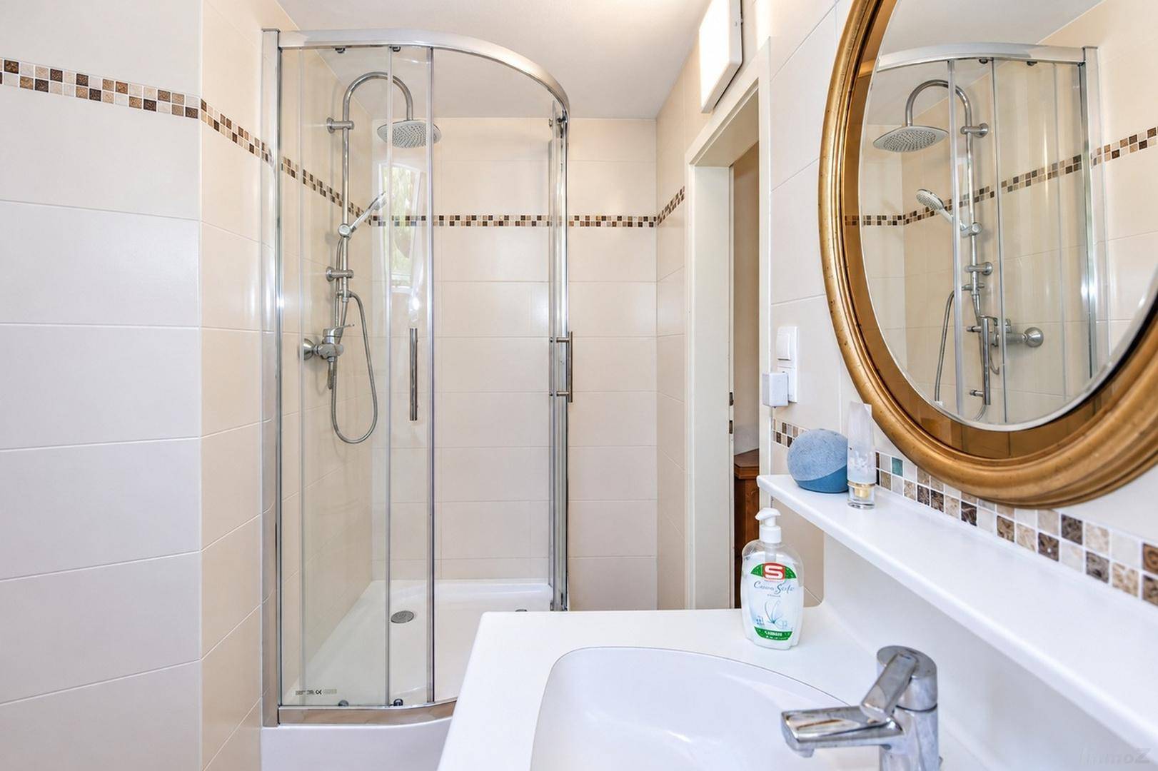 Modernes Badezimmer mit Duschkabine, Waschbecken und Spiegel, in hellen Fliesen gehalten.