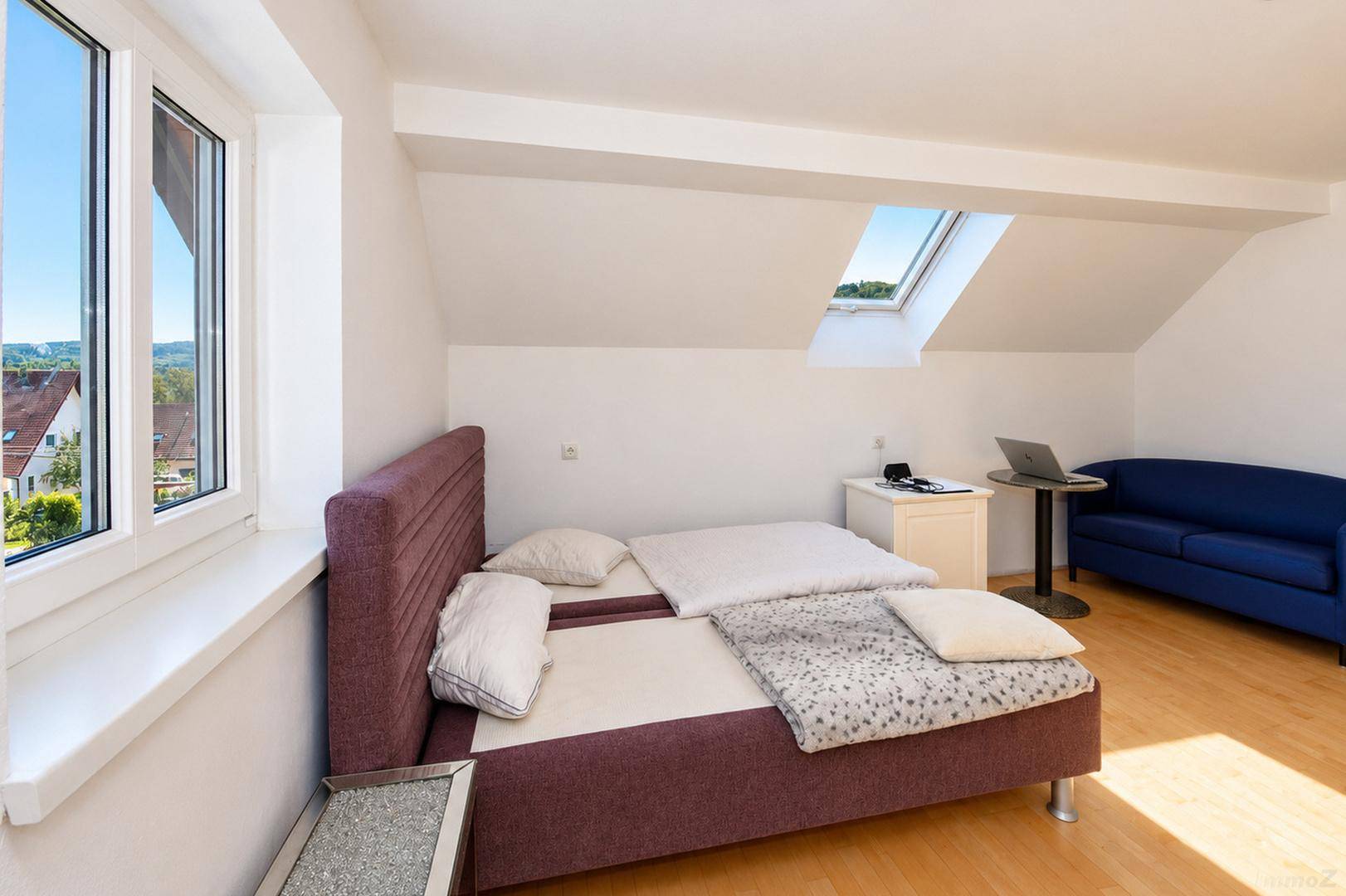 Gemütliches Schlafzimmer mit Sofa, Holzboden und weitem Blick ins Grüne durch das Fenster.