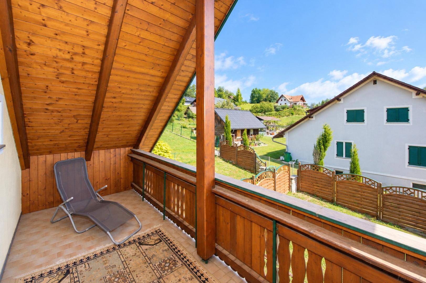 Überdachter Balkon mit Holzverkleidung, Liegestuhl und schöner Aussicht auf die umliegende Landschaft.