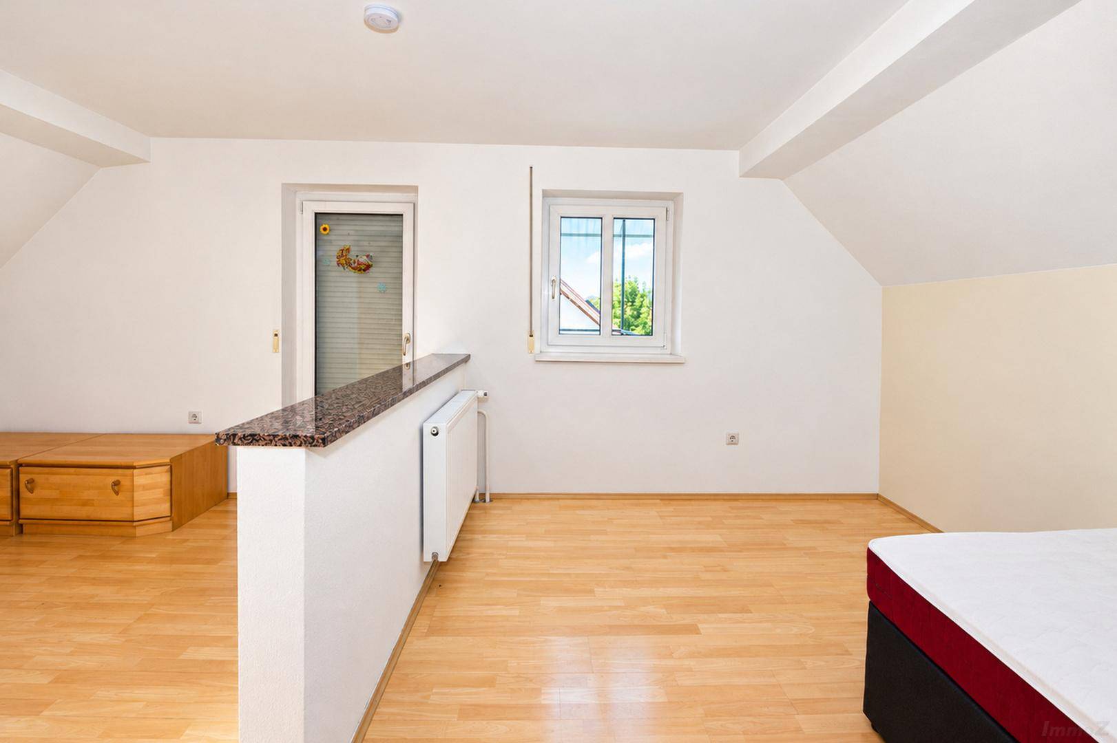 Schlafbereich mit Holzboden, Fenster und einem Raumteiler, der den Raum strukturiert.