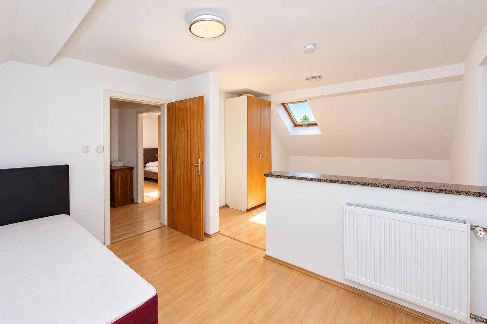 Schlafzimmer mit Holzboden, Raumteiler und Tür zu einem weiteren Schlafbereich im Dachgeschoss.