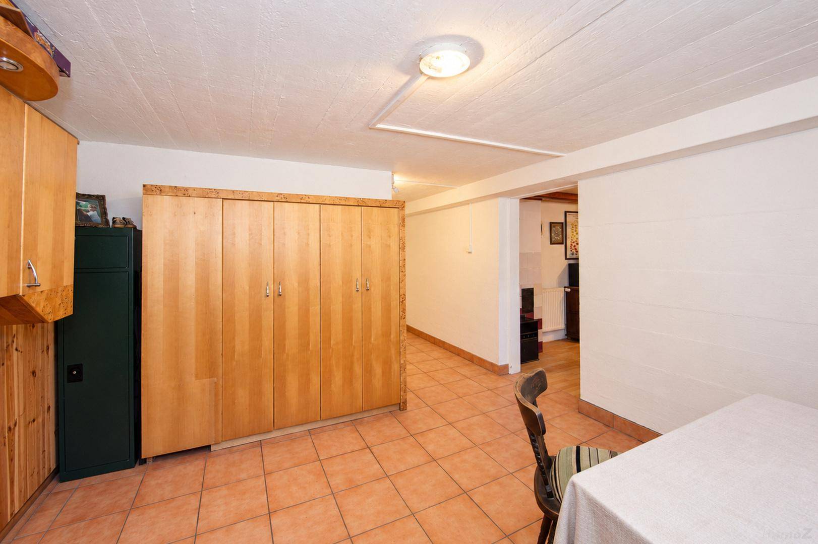 Kellerraum mit Fliesenboden und großem Holzschrank, bietet viel Stauraum.