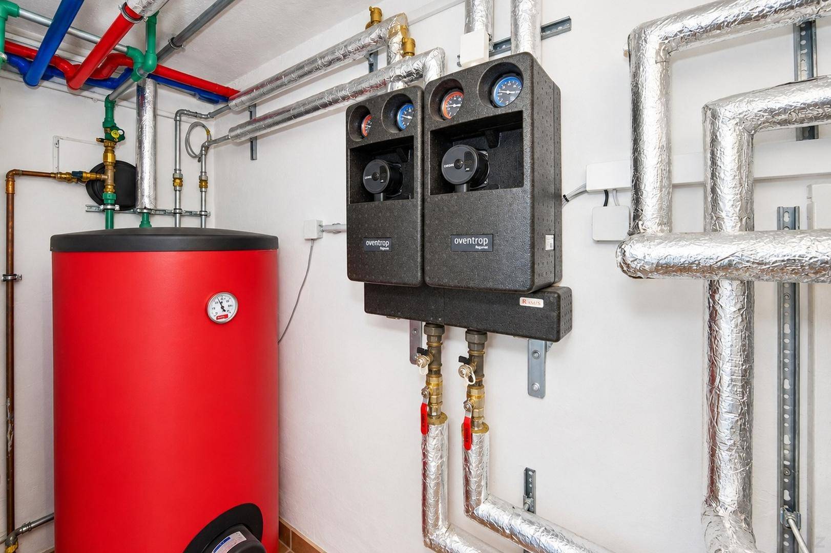 Moderner Heizungsraum mit Warmwasserspeicher und komplexem Rohrsystem für die Wärmeversorgung.