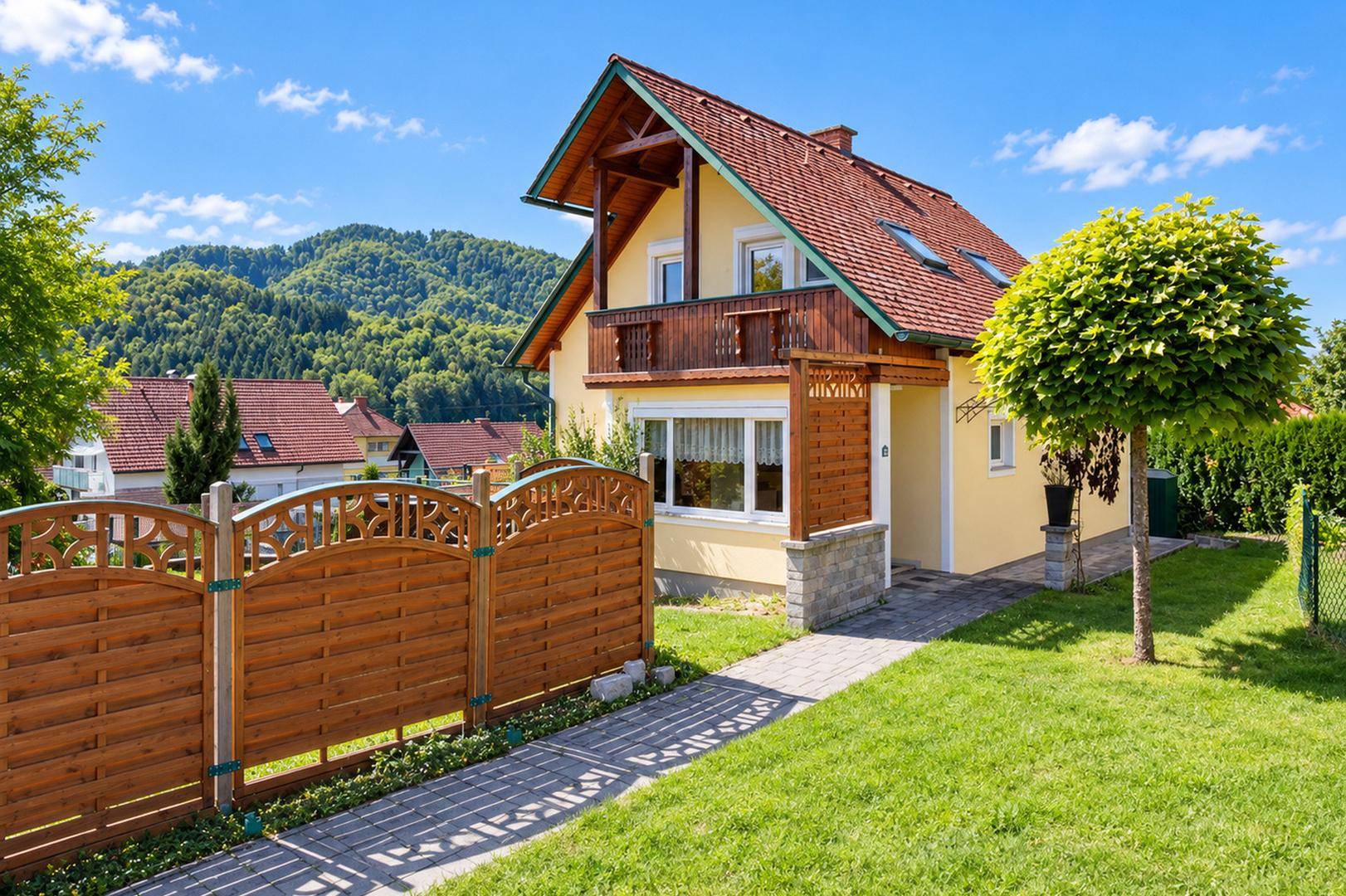 Charmantes Haus mit gepflegtem Garten, Holzzaun und malerischem Bergblick im Hintergrund.
