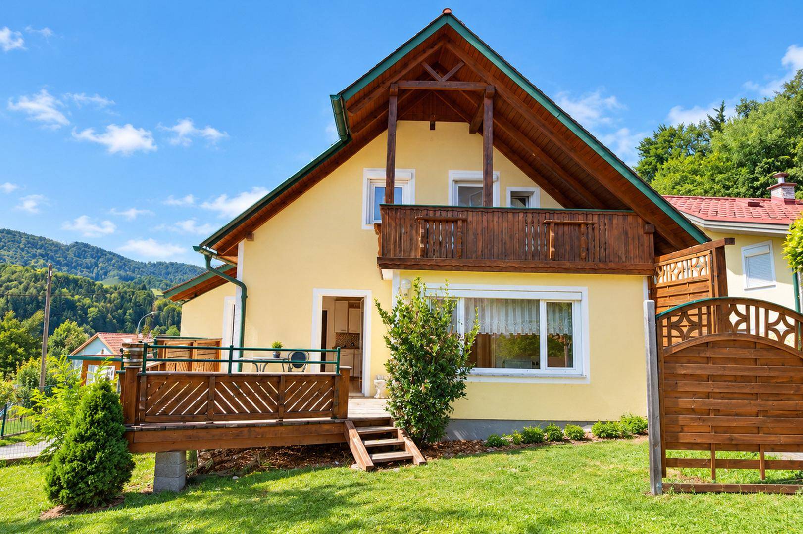Rückansicht des Hauses mit Holzterrasse, grünem Rasen und Zugang zum Garten.