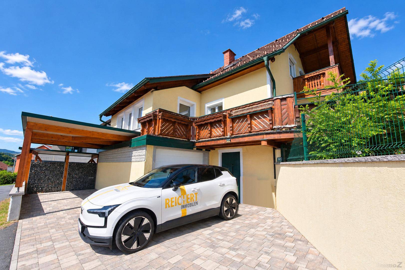 Ansicht des Hauses mit Carport, gepflasterter Auffahrt und einem geparkten Elektrofahrzeug.