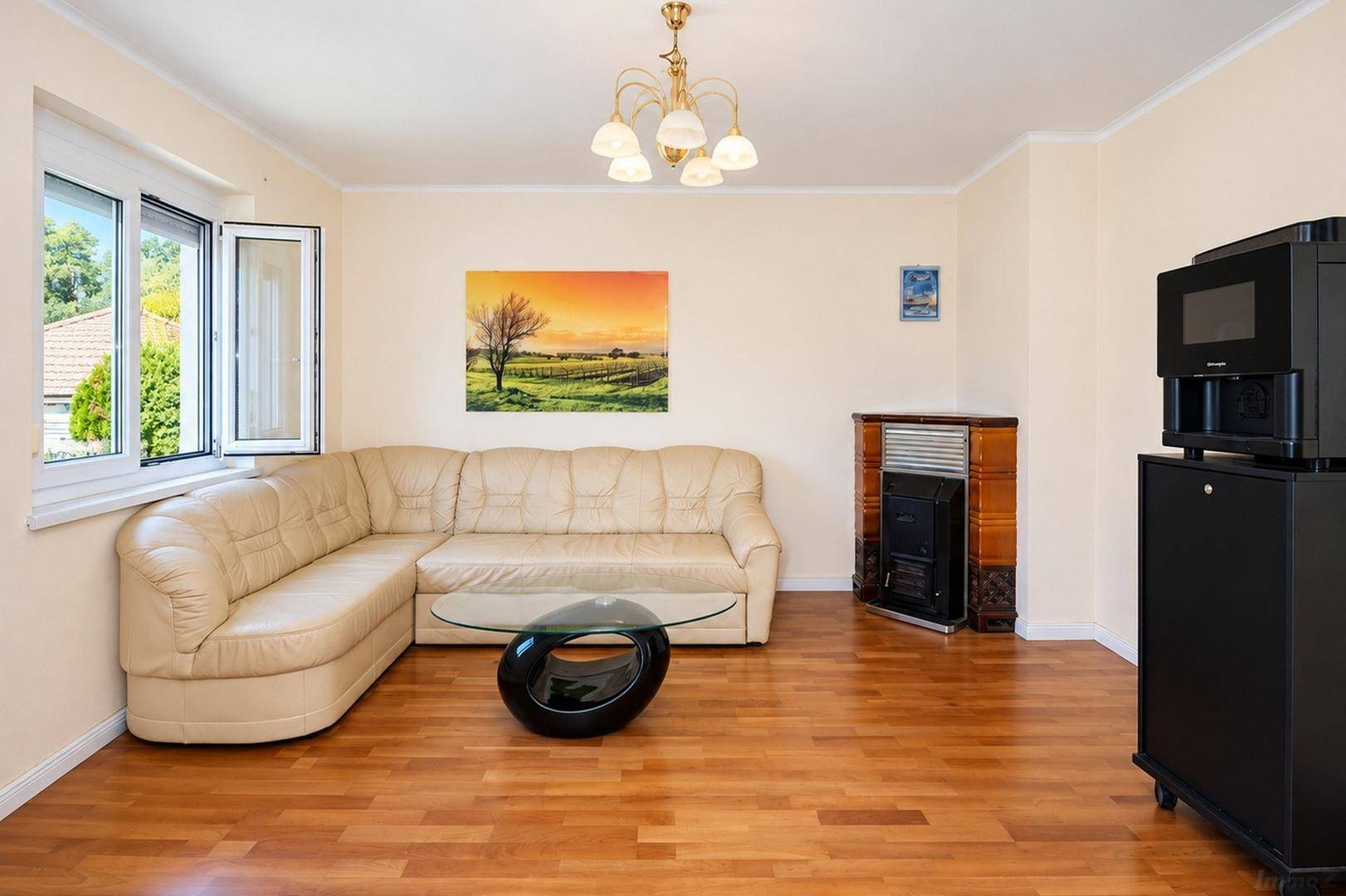 Wohnzimmer mit beigem Ecksofa, Kaminofen und Blick auf die umliegende Landschaft.