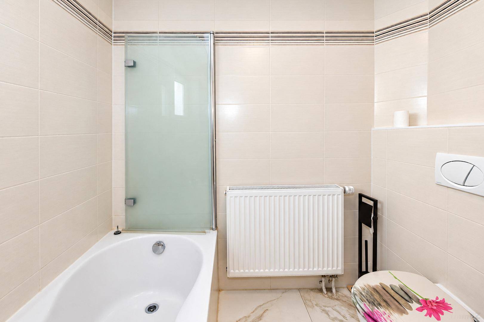 Badezimmer mit Badewanne, Duschabtrennung und Wand-WC, in neutralen Farben gefliest.