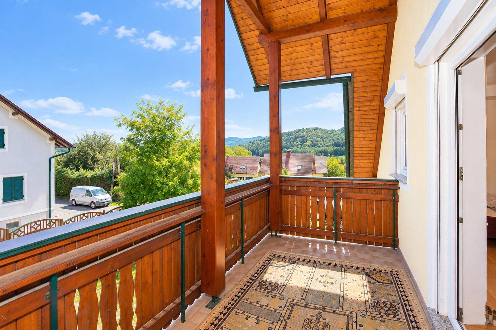 Geräumiger Holzbalkon mit Fliesenboden und weitem Blick über die grüne Umgebung.