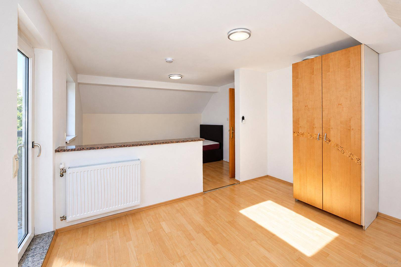 Geräumiger Raum mit Holzboden, Holzschrank und Zugang zum Balkon, hell und funktional.