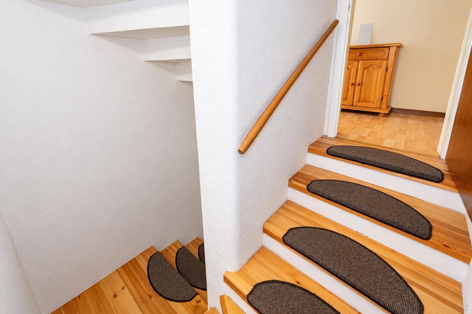 Holztreppe mit Teppichstufen und Holzgeländer, führt in den unteren Bereich.