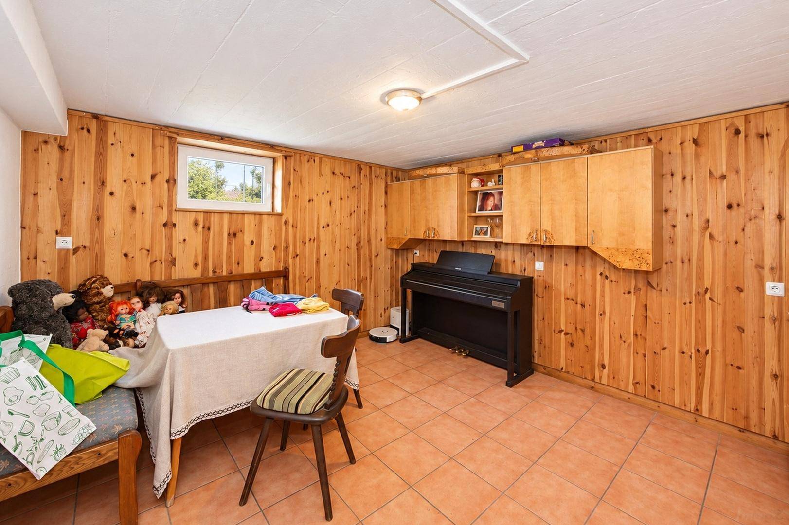 Gemütlicher Kellerraum mit Holzvertäfelung, Fliesenboden, Esstisch und Klavier.