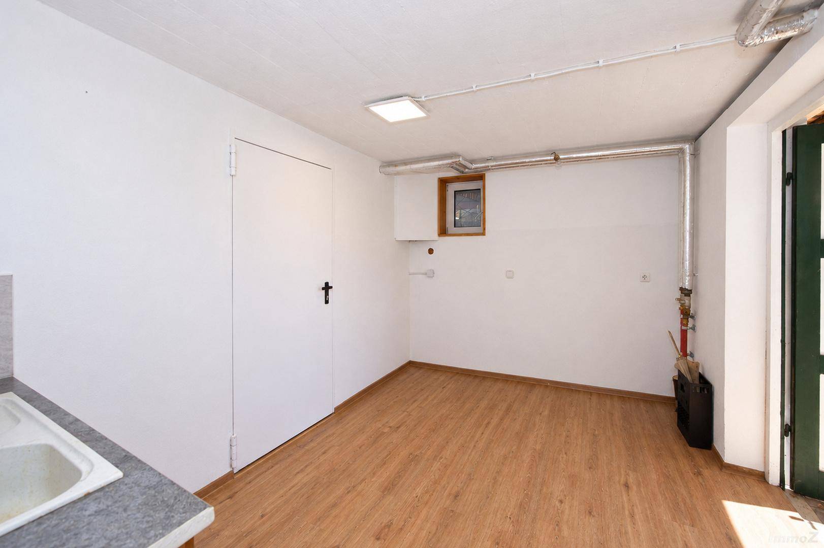 Funktionaler Raum mit Holzboden, weiß gestrichenen Wänden und kleinem Waschbecken.