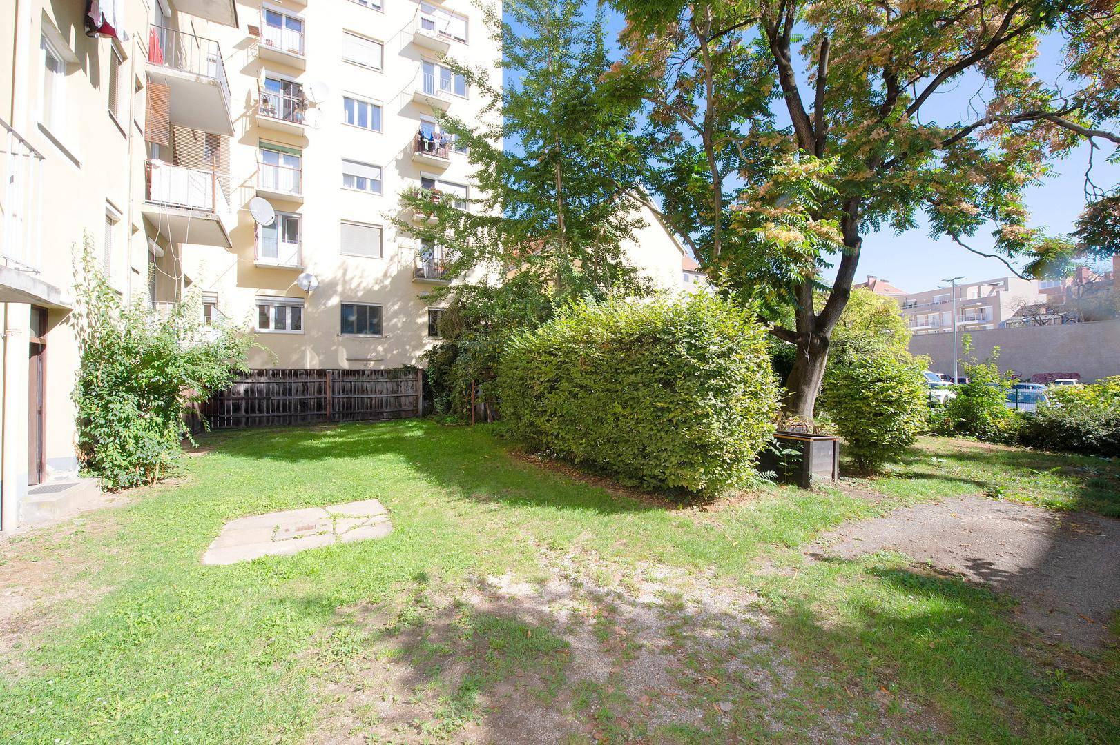 Gartenfläche mit Rasen und Hecken, angrenzend an ein Mehrfamilienhaus mit Balkonen.