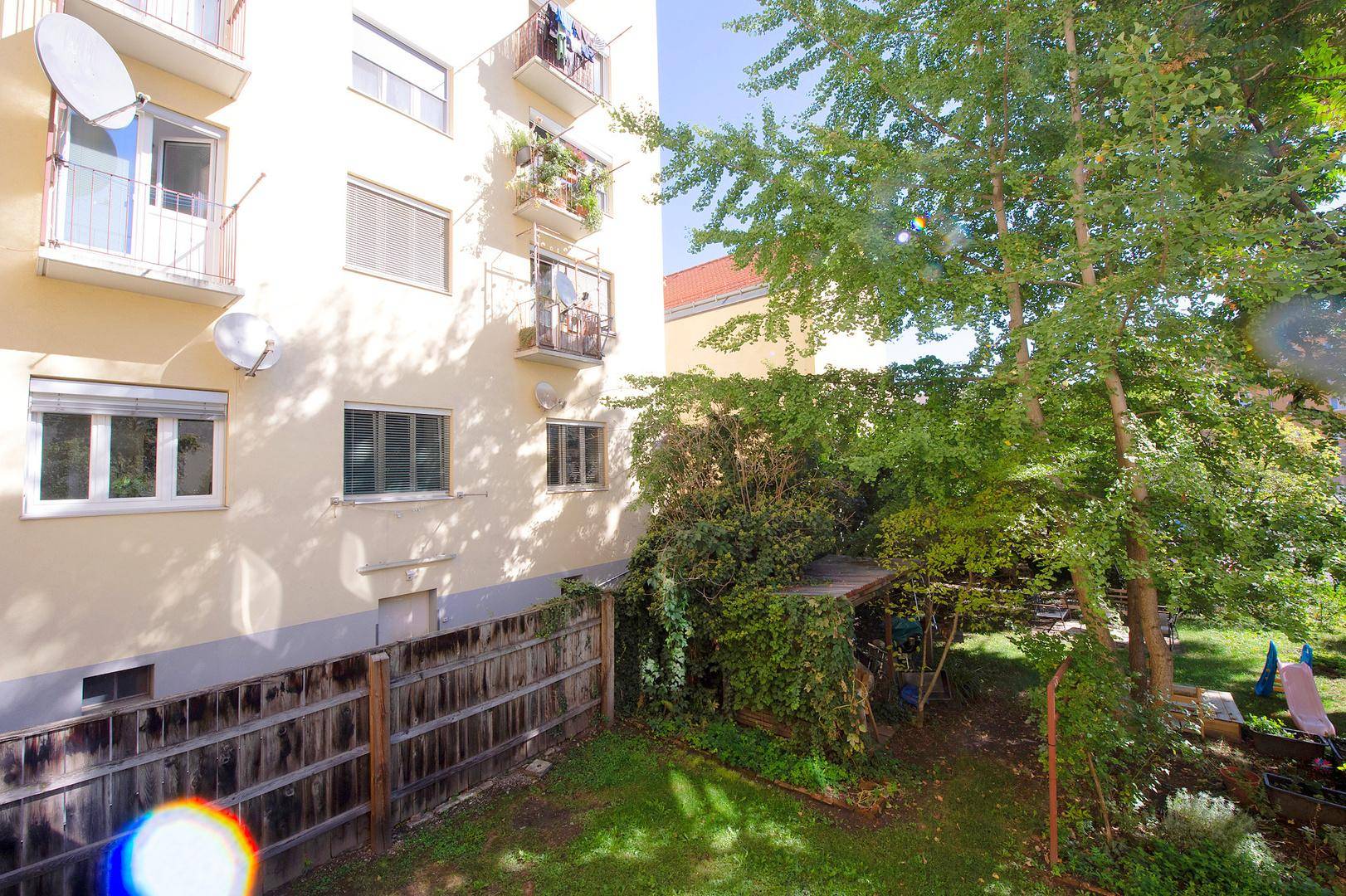 Blick auf den Gartenbereich und die Rückseite eines Wohngebäudes mit Balkonen und Fenstern.