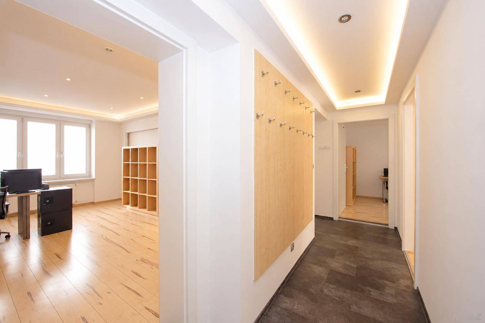 Heller Flur mit indirekter Beleuchtung, Garderobe und Blick in ein angrenzendes Büro.