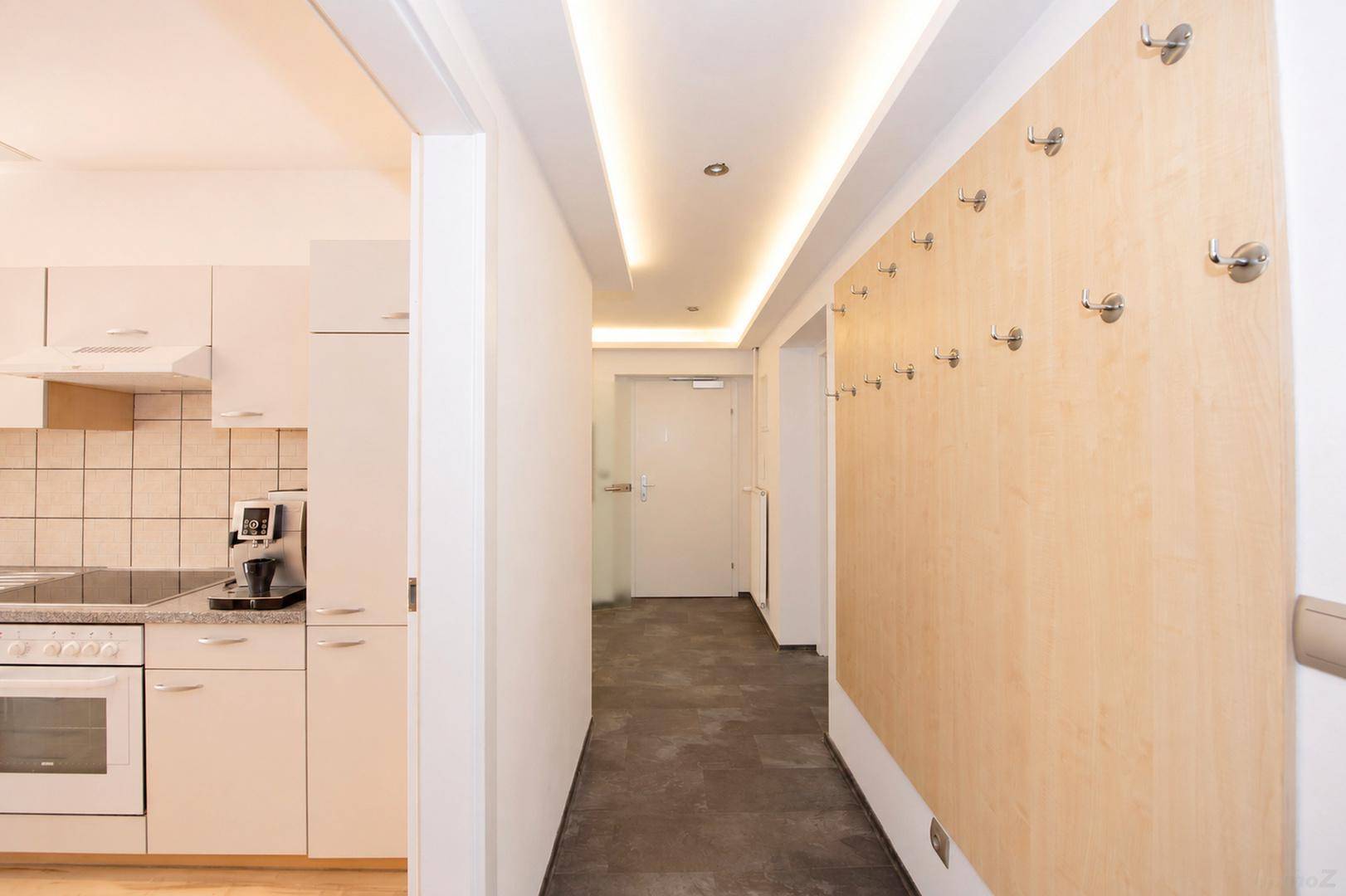 Heller Flur mit indirekter Beleuchtung, Garderobe und Blick in die angrenzende Küche.