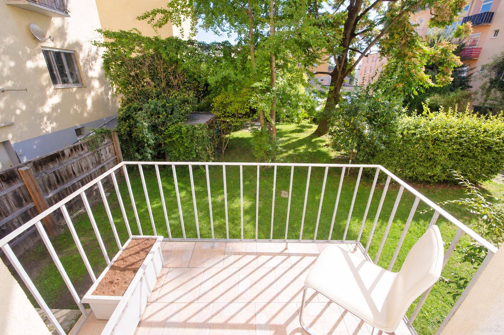 Kleiner Balkon mit Fliesenboden und Blick auf einen grünen Gartenbereich.