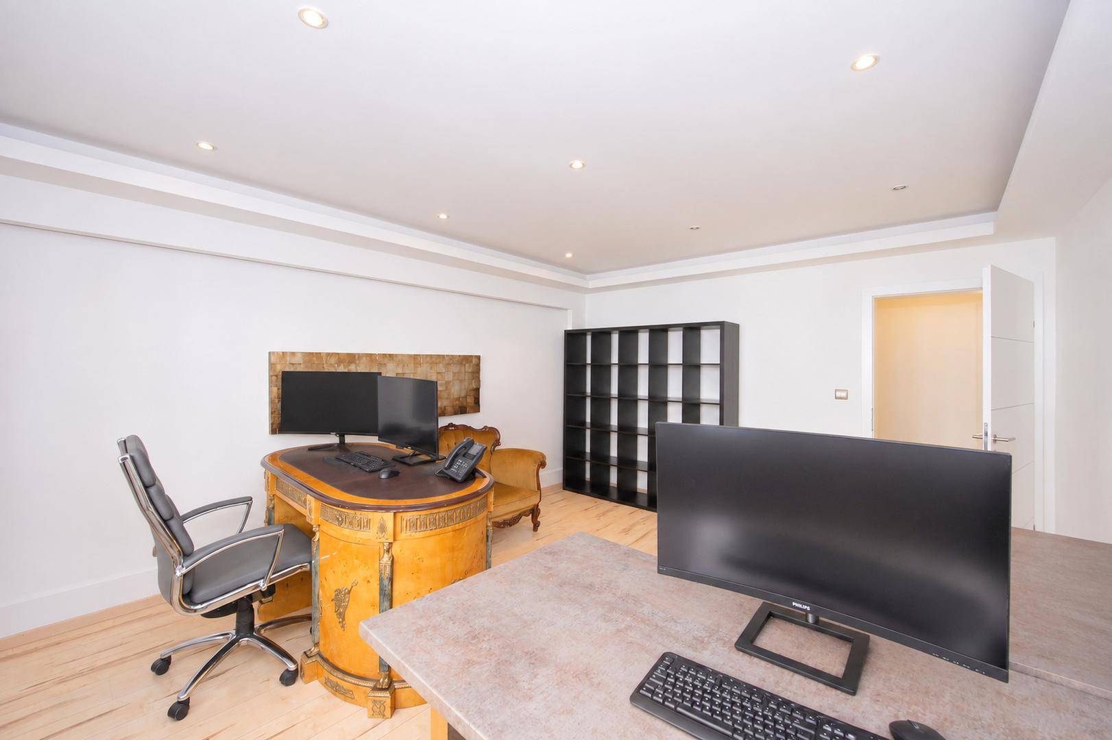 Modernes Büro mit mehreren Arbeitsplätzen, dunklem Regal und hellem Holzboden.