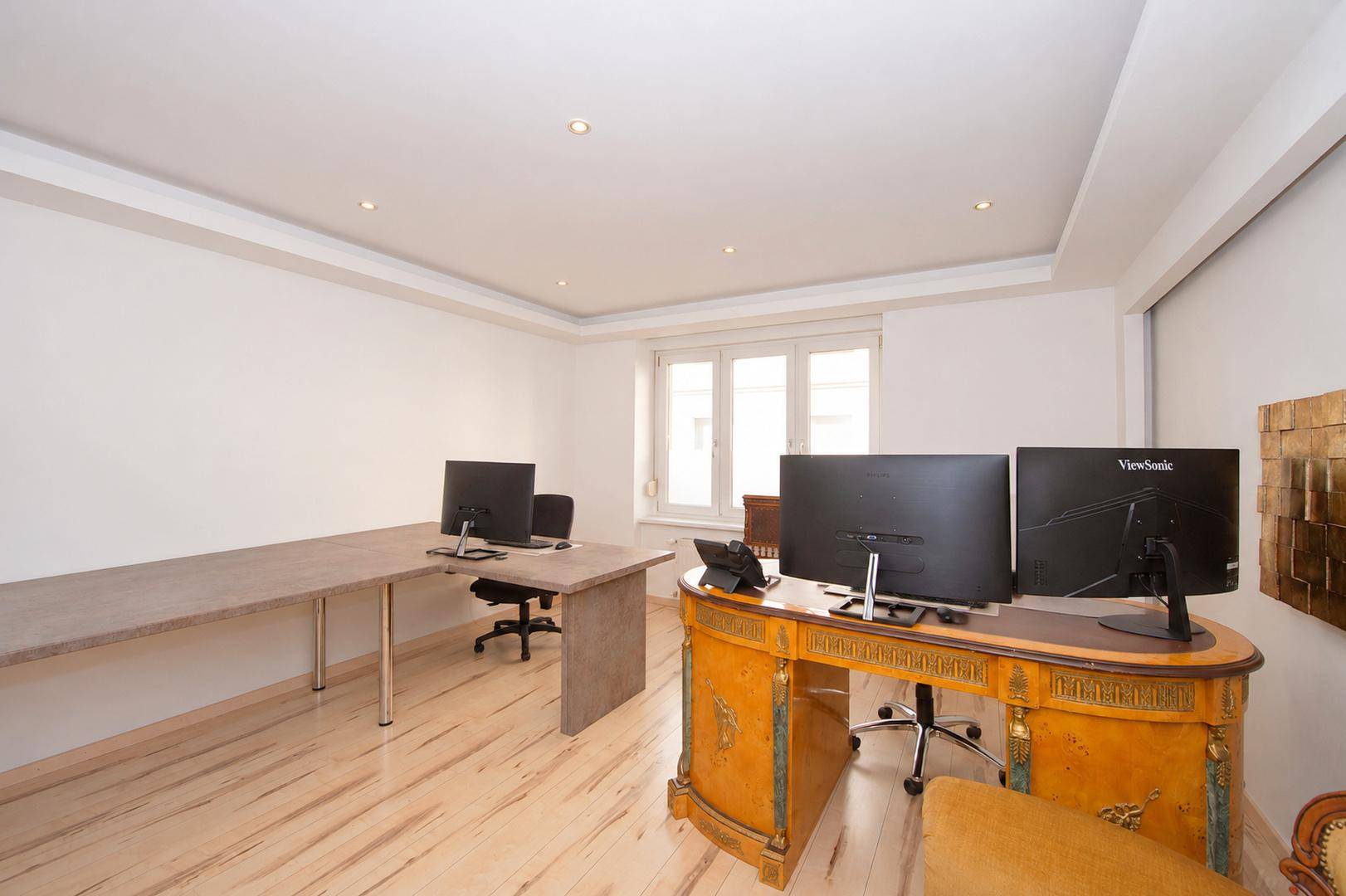 Geräumiges Büro mit zwei Arbeitsplätzen, hellem Holzboden und großen Fenstern.