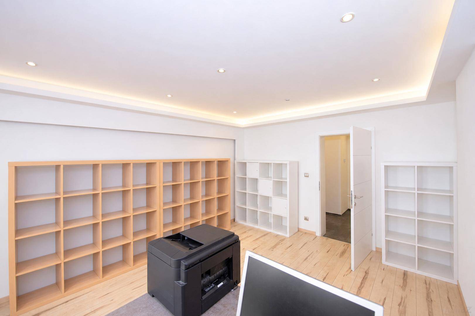 Helles Büro mit Holzboden, mehreren Regalen und einem Drucker, ideal für Arbeitsbereiche.