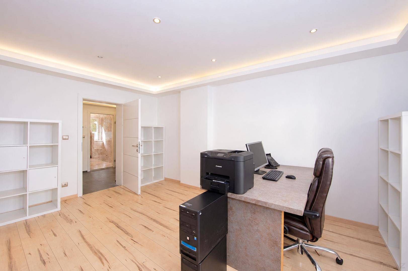 Modern eingerichtetes Büro mit Schreibtisch, Bürostuhl und Regalen, heller Holzboden.