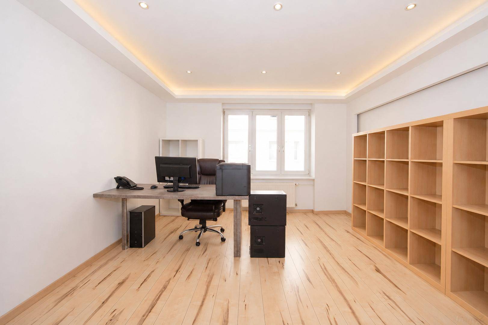 Geräumiges Büro mit hellem Holzboden, großem Fenster und modernen Regalsystemen.
