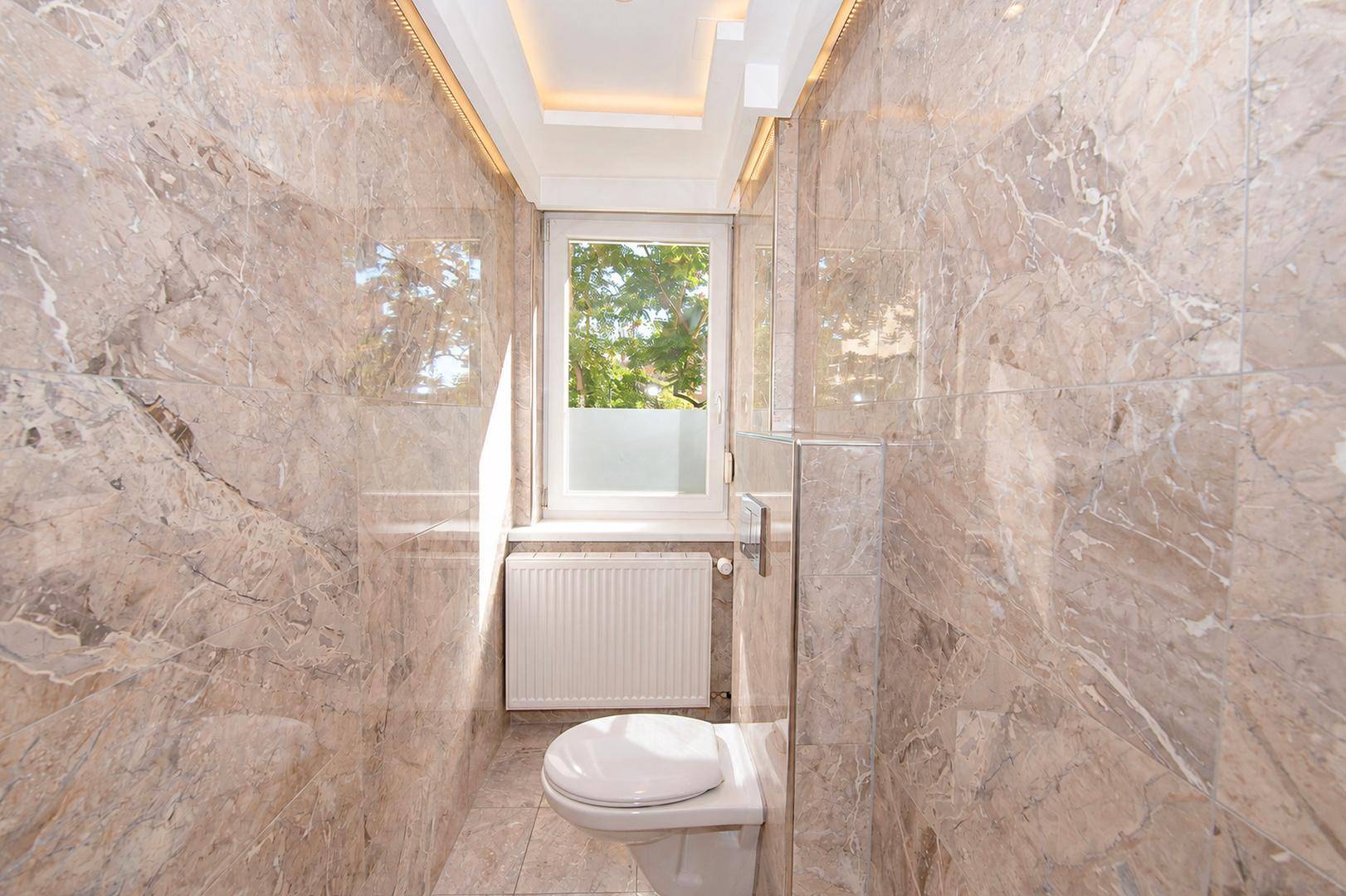 Separate Toilette mit eleganten Marmorfliesen, wandhängendem WC und Fenster für Tageslicht.