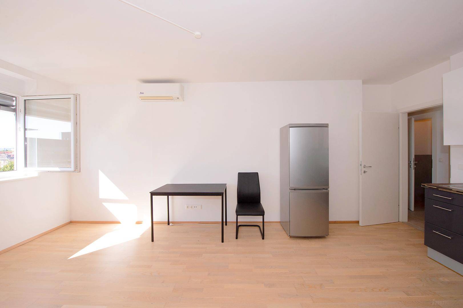 Sonniger Wohnbereich mit Esstisch, Kühlschrank und großem Fenster mit Blick nach draußen.