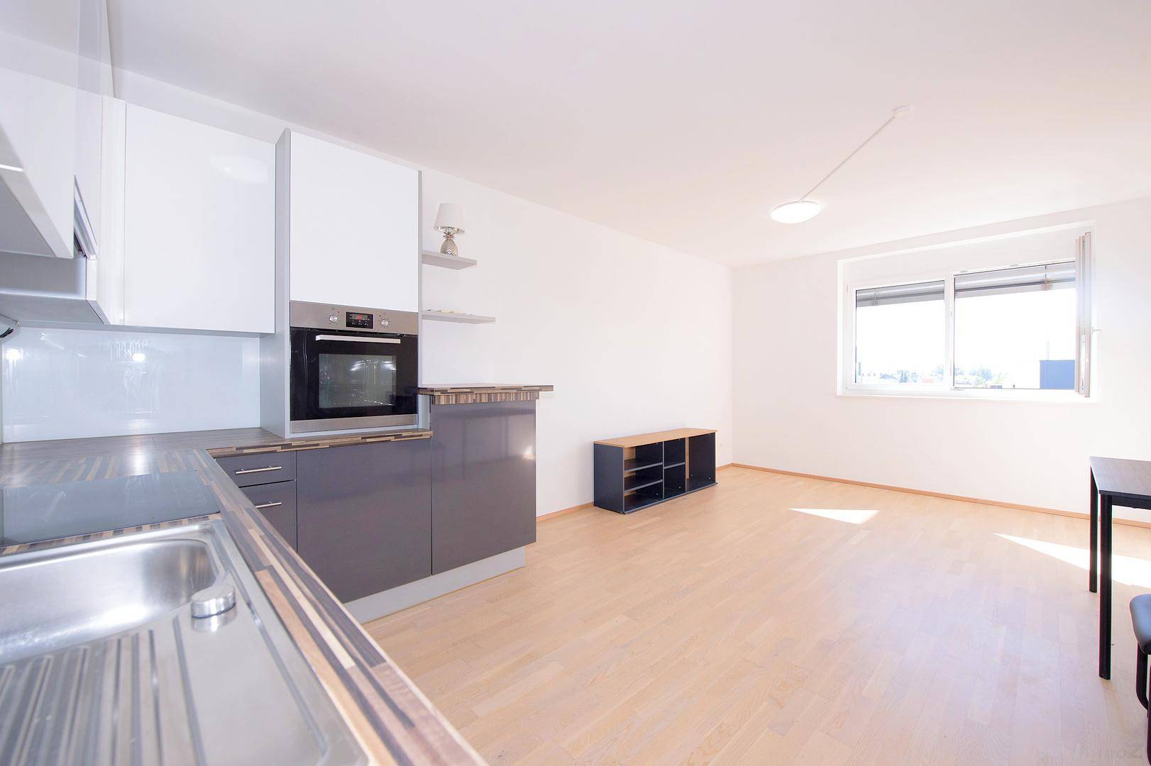 Offener Wohnbereich mit integrierter Küche, Parkettboden und großem Fenster für viel Licht.