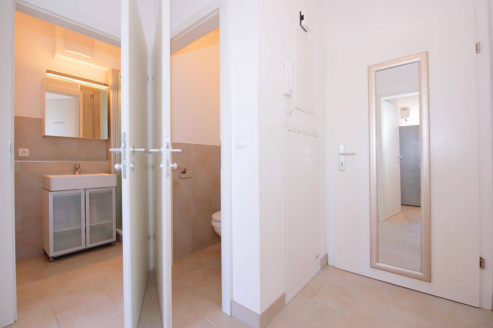 Heller Flur mit Zugang zu Badezimmer und separatem WC, ausgestattet mit Fliesenboden.