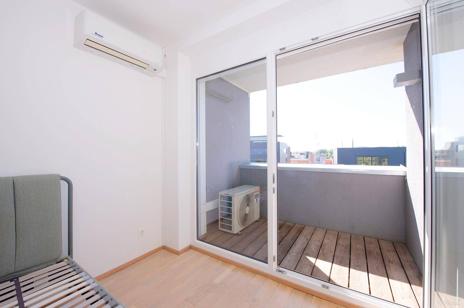 Kleiner Balkon mit Holzfußboden und Außeneinheit der Klimaanlage, sonnig und hell.