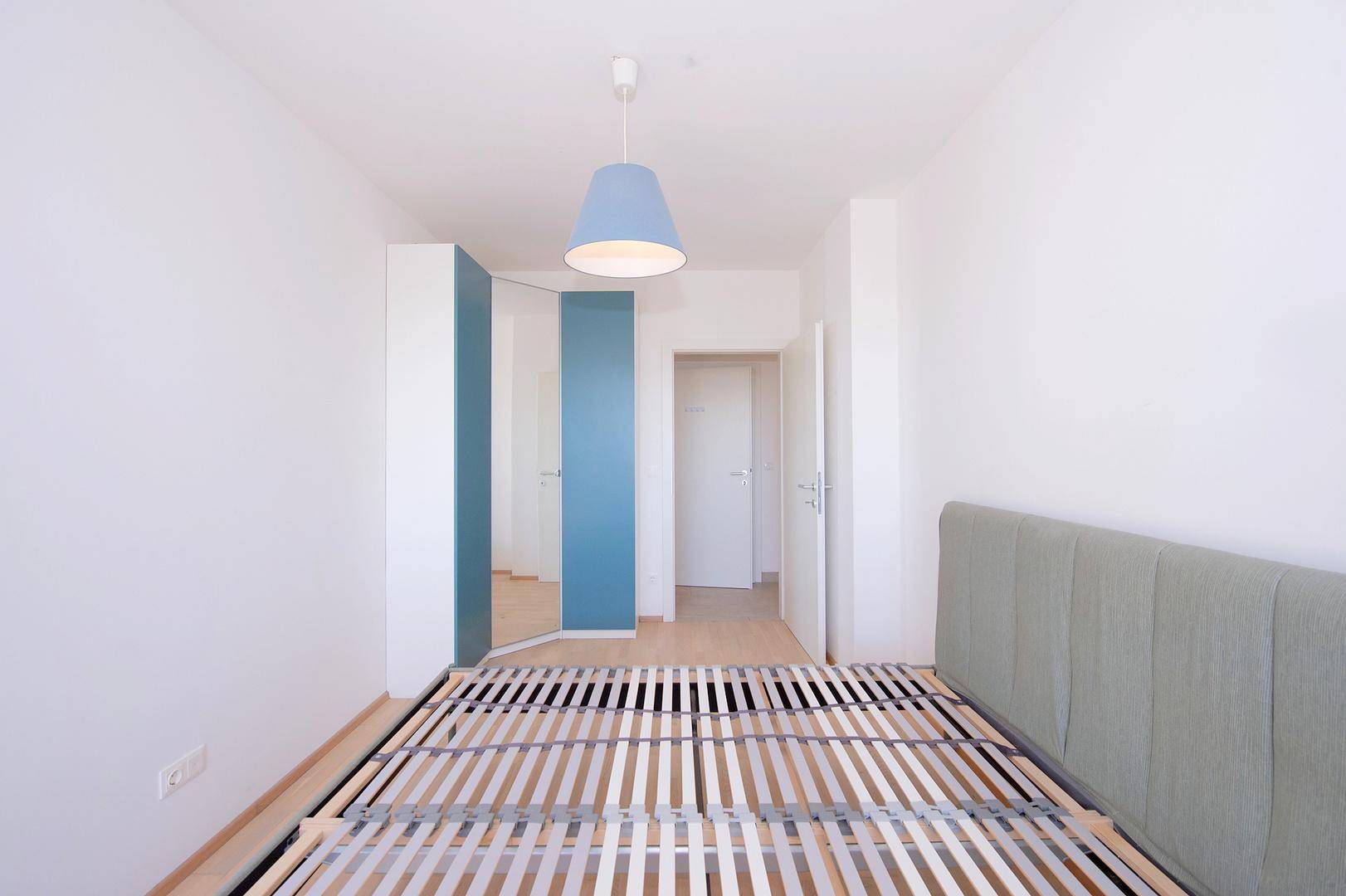 Geräumiges Schlafzimmer mit Bettrahmen, modernem Kleiderschrank und hellem Parkettboden.